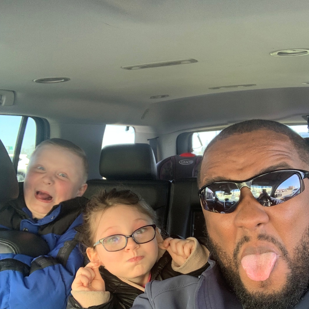 Anthony with two of his kids in the car, all making silly faces.