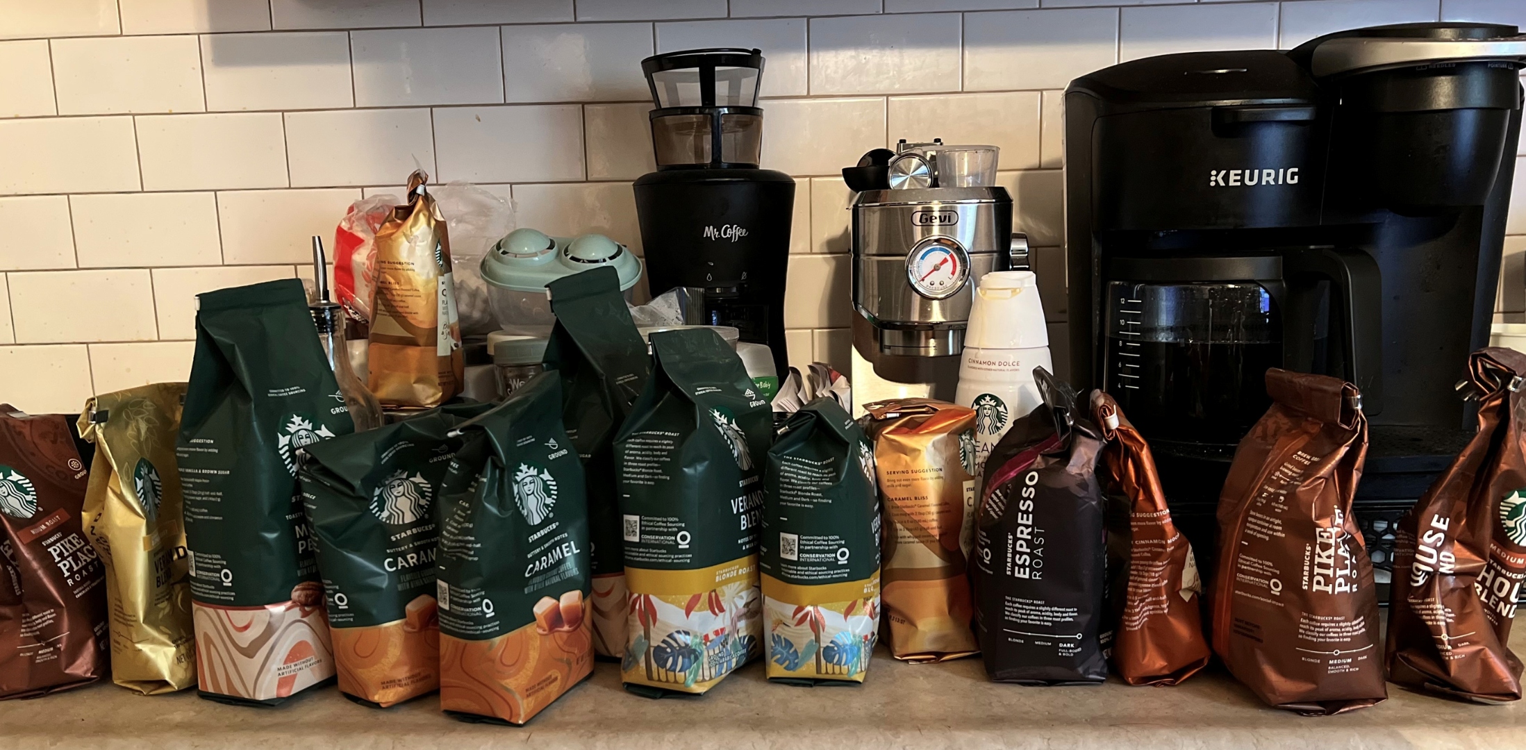 A row of Starbucks coffee bags lined up on a kitchen counter beside a Mr. Coffee brewer.