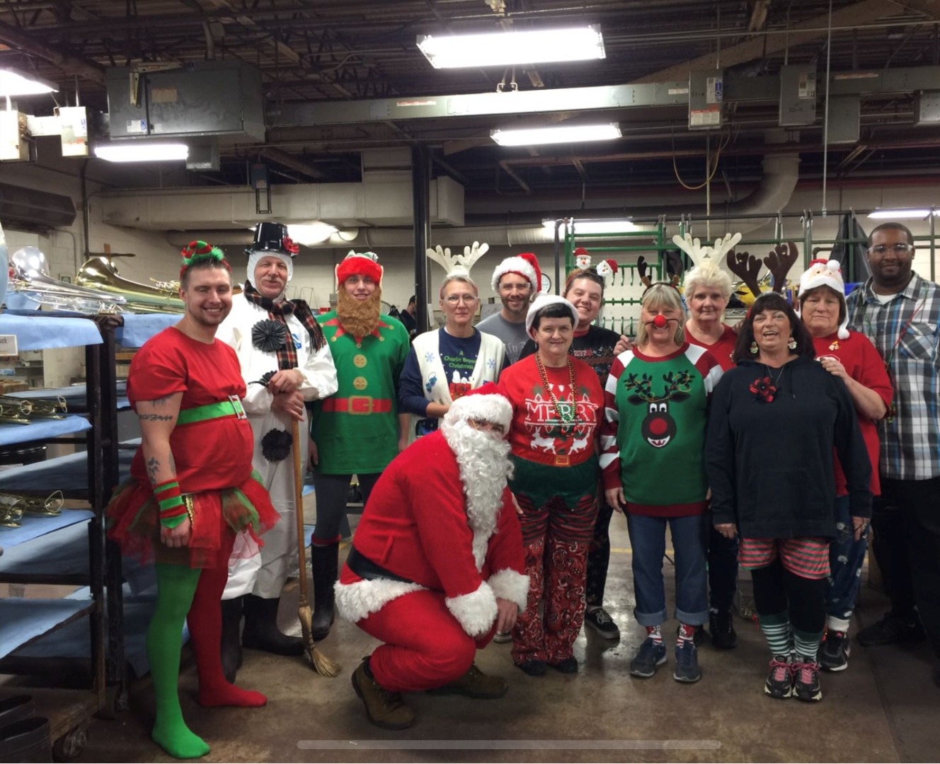 Conn-Selmer team in Christmas costumes on the plant floor with brass instruments visible.
